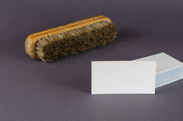 Garment cleaning brush and stack of blank business cards on gray background. Wooden brush with natural bristles and white rectangular business cards. Cleaning services, small business.