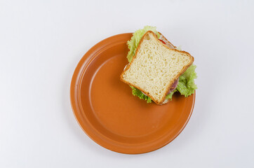 Brown clay plate and chopped ham sandwich on white background. S