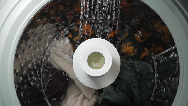 This slow motion , POV top view video machine shows a loaded washing machine with it's rinse cycle water running cascading into the machine.