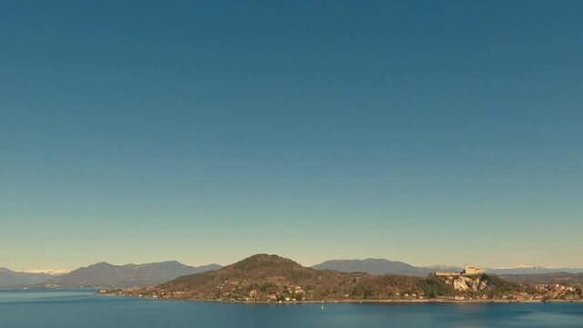 Panoramic view of beautiful lake Maggiore and Angera fortress with clear sky and boat sailing over calm waters. Panning