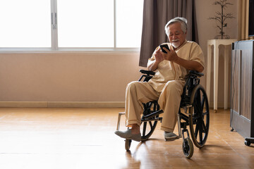 Asian elderly man sitting on wheelchair and using smart phone in patient room at the hospital. Patient man on wheelchair in room at hospital - obrazy, fototapety, plakaty