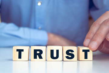 Businessman hand holding wooden cube block with TRUST business word on table background....