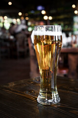 Glass of cold lager beer on bar or pub desk. Blurred backgrounnd of bar lights.