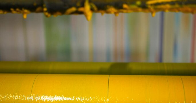 A slow motion close up of yellow coloured ink rollers and fast moving rolls of print in the background