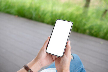 Mockup image of a woman holding mobile phone with blank white desktop screen in the outdoors