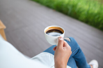 Closeup image of a woman holding and drinking hot coffee in the outdoors