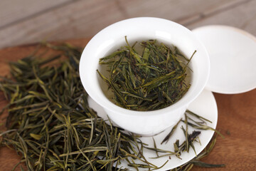Fototapeta premium Green tea leaves scattered on a cutting board and tea soup in a tureen
