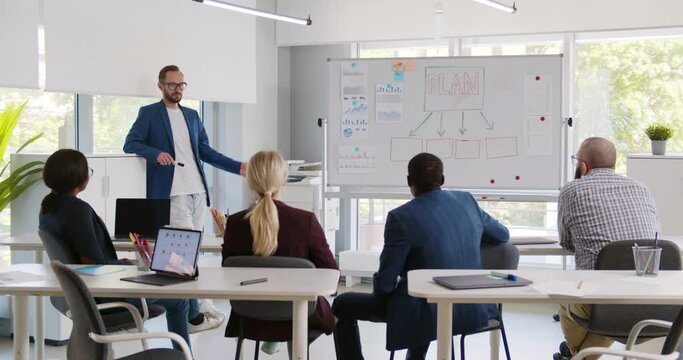 Man presenting report on whiteboard to diverse colleagues in business center