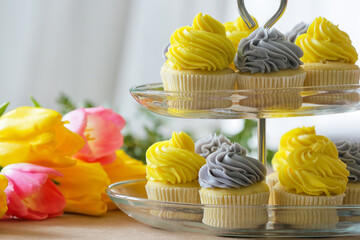 Dessert stand with tasty cupcakes and flowers on table, closeup