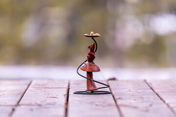 An isolated wooden mouse doll under a drip pan of a decorative burning candle stand against a blurry background. The figure of a mouse standing on its back paws under an umbrella.