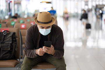 Young traveler man wearing mask protect flu coronavirus. Tourist in airport terminal using smartphone sitting and waiting his flight. During the pandemic must be social distancing self quarantine.