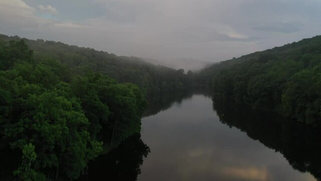Narrow forest river with rising fog in early summer morning, aerial view