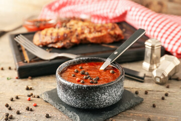Bowl with peppercorn sauce and roasted meat on wooden background