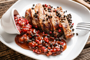 Plate with tasty roasted meat and peppercorn sauce on wooden background, closeup
