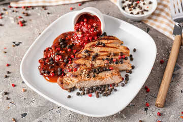 Plate with tasty roasted meat and peppercorn sauce on grunge background