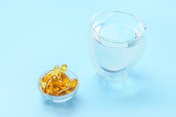 Bowl with fish oil capsules and glass of water on color background