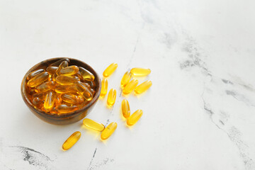 Bowl with fish oil capsules on light background