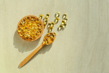 Bowl and spoon with fish oil capsules on grey background