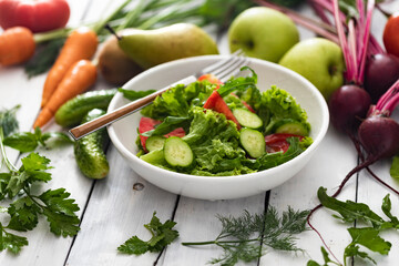 Bowl with fresh summer salad and ingredients on white wooden table, healthy food