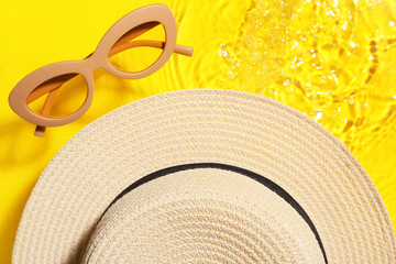 Stylish hat and sunglasses in water on color background, closeup