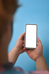 Rear view young man holding mock up smart phone over blue background.