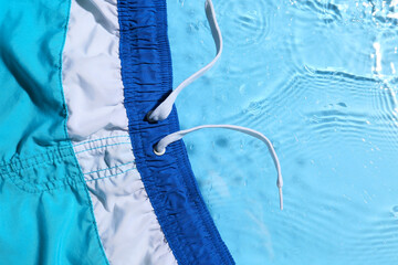 Male swimming trunks on color background with water splashes