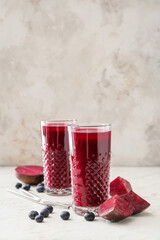 Glasses of healthy smoothie with beetroots and blueberries on light background