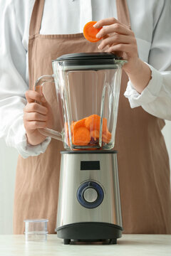 Woman preparing tasty carrot smoothie in kitchen