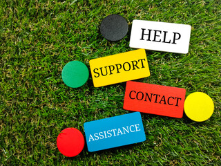 Text HELP SUPPORT CONTACT ASSISTANCE on colorful wooden board on green grass background.