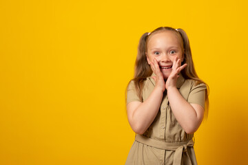 Portrait of surprised cute little girl child isolated over yellow background.  Hands near open...