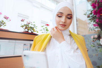 Young muslim woman in hijab using her smartphone in cafe