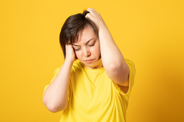Fototapeta premium Upset exhausted woman suffers from terrible migraine, massages temples, grimaces because of pain, tired after working, closes eyes, wears yellow t shirt. Negative feelings
