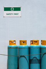 Gas cylinder tanks with safety first sign on white cement wall in safety zone area outside of...