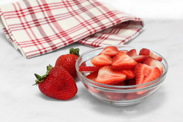 A glass bowl of sweet sliced strawberries with whole berries to the side.