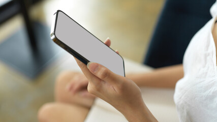 Side view of female hand holding smartphone with mock-up screen in workplace