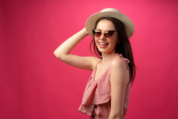 Studio fashion portrait of a young attractive woman in hat and glasses against pink backgorund