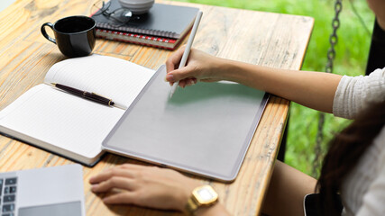 Cropped shot of female hand using digital tablet and stationery on the table