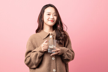 Beautiful woman drinking water on pink background