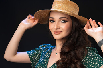 Beautiful young woman with straw hat posing against black background