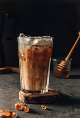 Iced coffee in a tall glass with cream poured over. Dark mood background. Selective focus