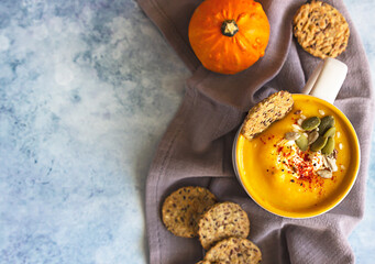 Pumpkin cream soup with seeds and cream in ceramic mug and multigrain healthy crackers. Top view.