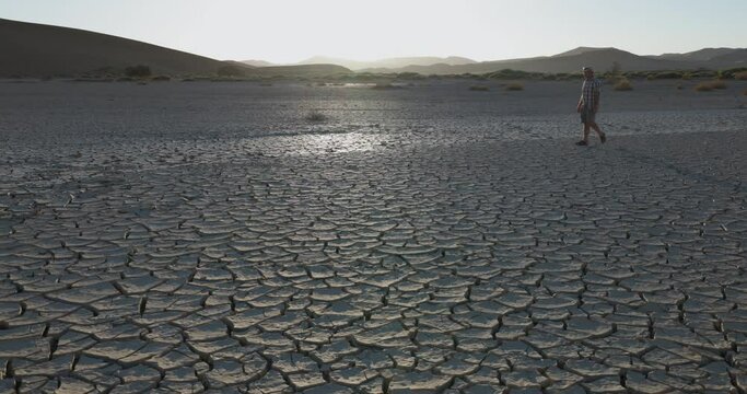 Climate change.Devastated farmer walking across the patterned cracked mud surface of a dry dam due to drought from climate change and global warming