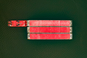 One tug towing pushing three barges with bulk cargo on the river.