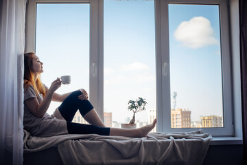 Silhouette of young slender girl sitting on the windowsill at home, side view, copy space. Outside...