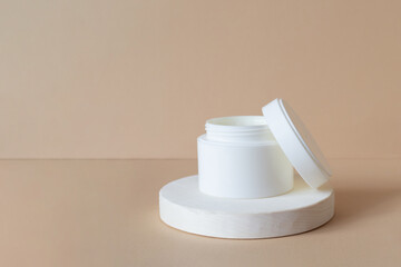 White cosmetic jar with cream on wooden geometric stand, 3d podium for presentation of the product packaging. Close-up, beige pastel background. Mockup for beauty industry