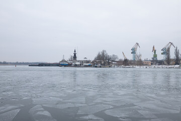 A river with floating melting pieces of ice. There are many construction cranes and tower on the shore. Ukraine