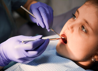 Close up of dentist in sterile gloves examining child teeth with dental explorer and mirror....