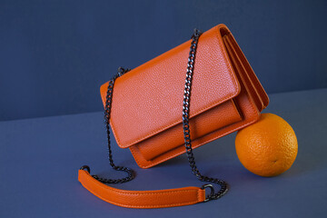 Bright orange leather women's handbag and orange fruit on dark fabric background. Fashion and shopping concept