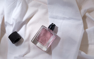 beauty, perfumery and object concept - bottle of perfume and cap on white sheet with folds
