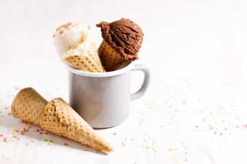 Ice cream scoops in cones on white wooden background.